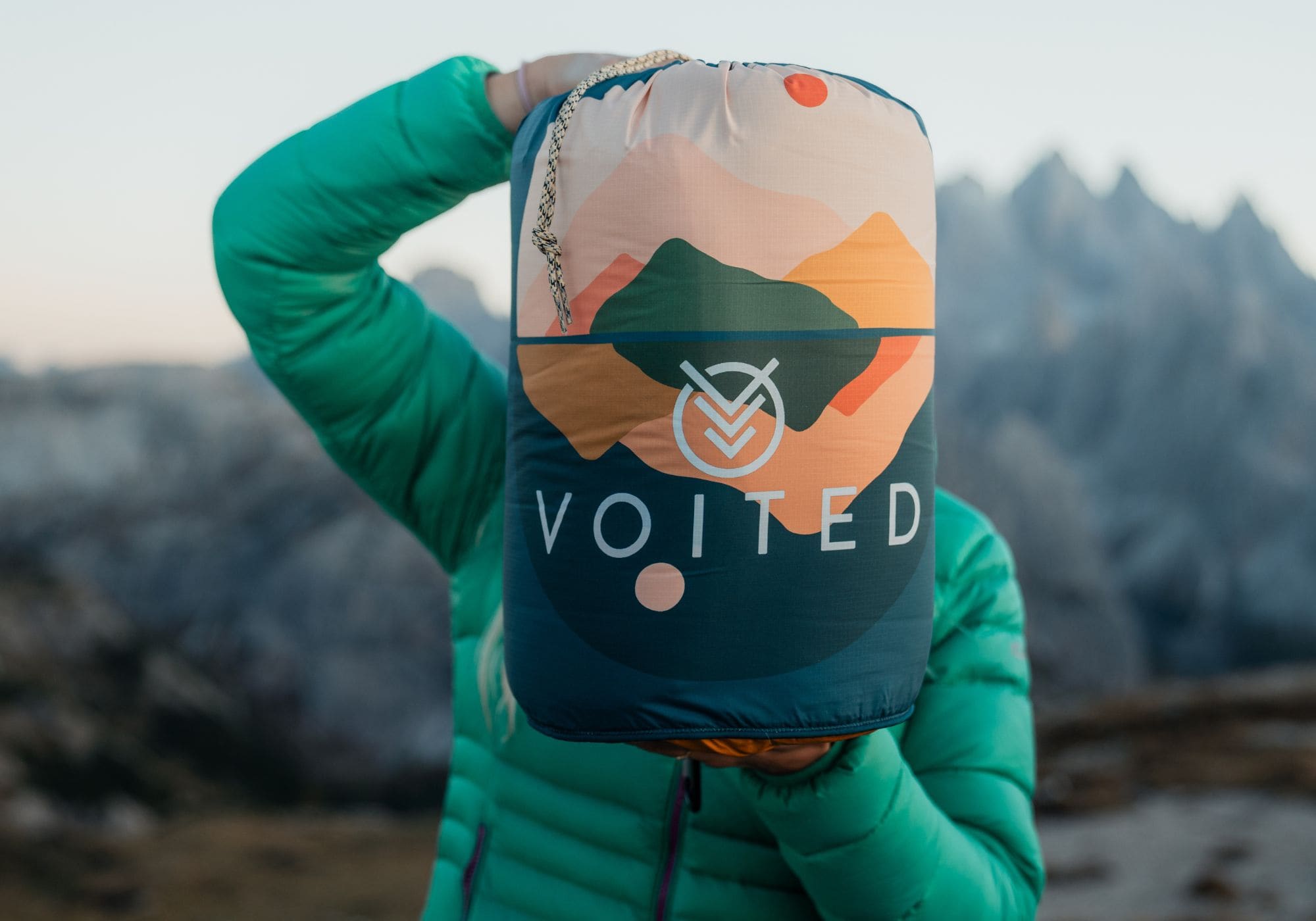 Sac de compression VOITED à imprimé montagne tenu devant le visage, sommets enneigés en arrière-plan Cloudtouch