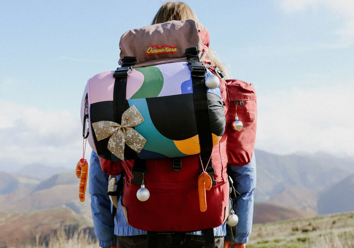 Randonneuse en montagne avec une couverture VOITED Cloudtouch colorée sur un sac à dos décoré pour Noël.