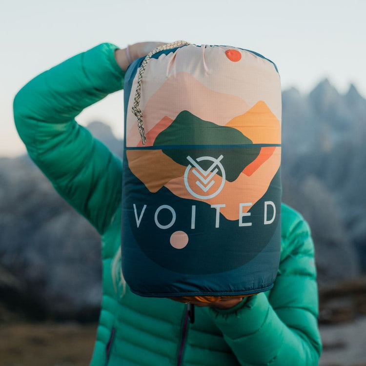 Sac de compression VOITED à imprimé montagne tenu devant le visage, sommets enneigés en arrière-plan Cloudtouch